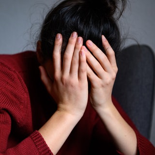 Eine Frau sitzt mit dem Kopf in den Händen auf einem Stuhl. der Weisse Ring berichtet über die Scham der Opfer. (Symbolbild)
