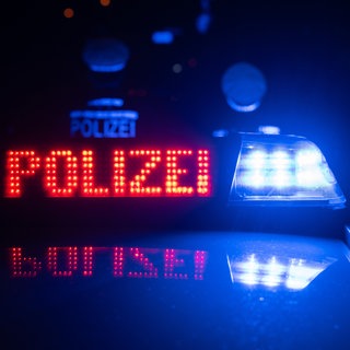 Zwei Polizisten stehen nachts vor einem Polizeiauto (Symbolbild). In der Nacht gab es einen Einbruch in einen Supermarkt in Eppingen. Ein Tresor wurde geknackt. 