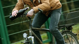 Mit einer Flasche Bier in Händen fährt ein junger Mann Fahrrad