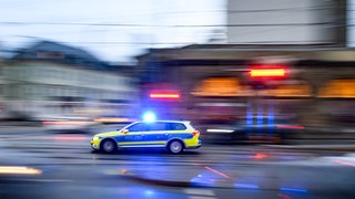 Ein Polizeiauto fährt mit Blaulicht über eine Kreuzung (Symbolbild). Nach einem Supermarkt-Klau ist in Crailsheim ein Ladendieb von einem Auto erfasst worden. 