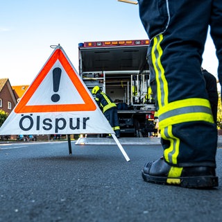Ein Feuerwehrmann steht neben einem Warnschild mit der Aufschrift «Ölspur». 