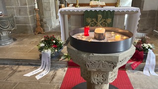 Vor dem Altar in der evangelischen Laurentiuskirche Niedernhall haben viele Menschen Blumen niedergelegt und Kerzen aufgestellt.