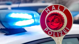 Eine Warnkelle vor einem Streifenwagen (Symbolbild). In Rot am See haben Polizisten einen älteren Autofahrer gestoppt. Seine 88-jährige Beifahrerin ging daraufhin auf die Beamten los.
