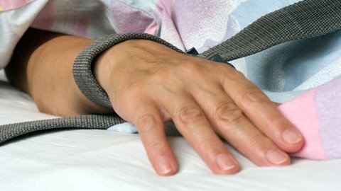 Patient mit Gurt am Bett fixiert (Symbolbild). Die Anwendung von Zwang in der Psychiatrie ist für alle Beteiligten belastend. Jeder Fall wird am ZfP Weinsberg aufgearbeitet.