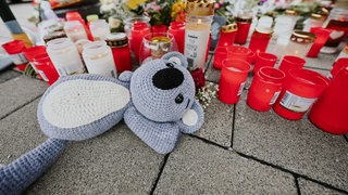 Ein Plüschtier, Blumen und Kerzen liegen auf dem Parkplatz eines Supermarktes. Nach dem Tod des 12-Jährigen trauern die Schüler und Lehrer um ihren Mitschüler.