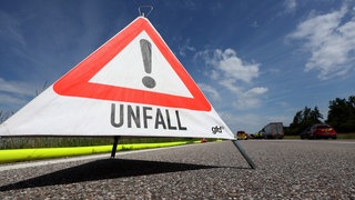 Ein Warndreieck mit der Aufschrift "Unfall" steht auf einer Autobahn (Symbolbild).