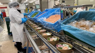 Mitarbeiter befüllen Schüsseln mit Salat.