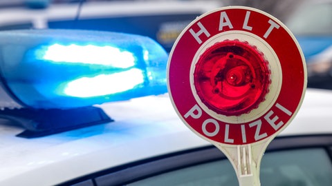 Eine Kelle vor reinem Polizeiauto mit Blaulicht (Symbol): Ein 78-jähriger Autofahrer war am Donnerstag unter Einfluss von Drogen in Gaildorf (Kreis Schwäbisch Hall) unterwegs. Dabei hat er nicht nur ein wartendes Auto beschädigt.