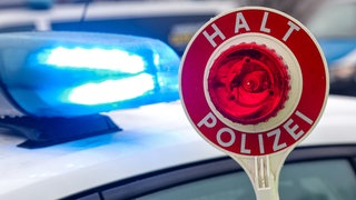 Eine Kelle vor reinem Polizeiauto mit Blaulicht (Symbol): Ein 78-jähriger Autofahrer war am Donnerstag unter Einfluss von Drogen in Gaildorf (Kreis Schwäbisch Hall) unterwegs. Dabei hat er nicht nur ein wartendes Auto beschädigt.
