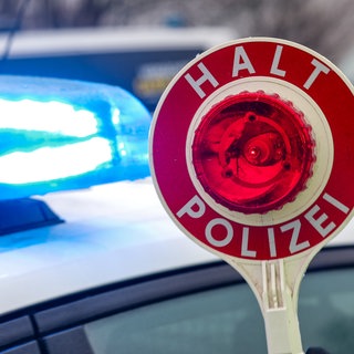 Eine Kelle vor reinem Polizeiauto mit Blaulicht (Symbol): Ein 78-jähriger Autofahrer war am Donnerstag unter Einfluss von Drogen in Gaildorf (Kreis Schwäbisch Hall) unterwegs. Dabei hat er nicht nur ein wartendes Auto beschädigt.