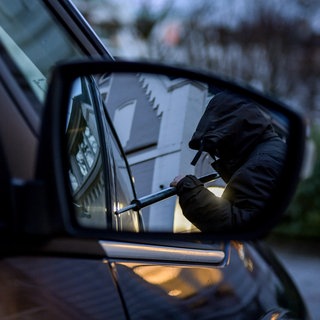 Ein Dieb will ein Auto aufbrechen (Symbol): Mehr als 30 Autos wurden zwischen Januar und Juli 2024 in Baden-Württemberg gestohlen. Die Polizei hat nun zwei mutmaßliche Haupttäter festgesetzt.