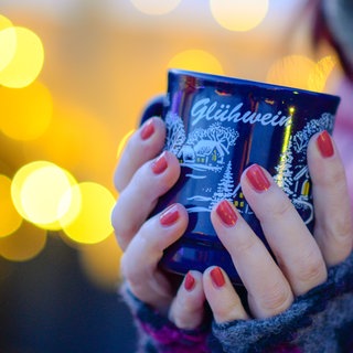 Eine Frau hält auf dem Weihnachtsmarkt eine Tasse mit Glühwein. Insassen der Heilbronner JVA haben jetzt bereits den Glühwein der eigenen Produktion abgefüllt.