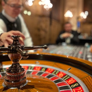 Ein Roulettetisch in einem Casino, im Hintergrund sind unscharf ein Croupier und ein Gast zu sehen.