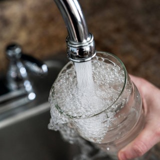 Symbolbild Wasserverseuchung mit PFAS: Wasser fließt aus einem Wasserhahn in ein Glas