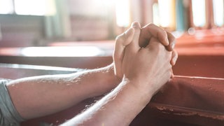 Betende Hände auf Kirchenbank