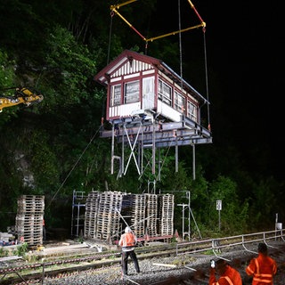 Das Gebäude des Stellwerks in Calw wird an einer Bahnstrecke von einem Kran über die Gleise gehoben.