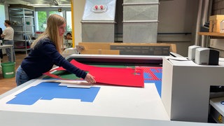 Ausbildung zum Papiertechnologen im Papierzentrum in Gernsbach: Azubi Saphira beugt sich über einen Tisch mit bunten Kartons.