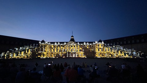 Bei bestem Sommerwetter haben die Schlosslichtspiele Karlsruhe begonnen. Schlossfassade mit Videoinstallation, davor Publikum.