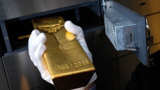 (Symbolbild) Eine Hand schiebt einen Goldbarren in ein Tresor. Unbekannte stehlen in Bruchsal Gold im Millionenwert. Sie hatten sich vorher als falsche Polizisten ausgegeben.