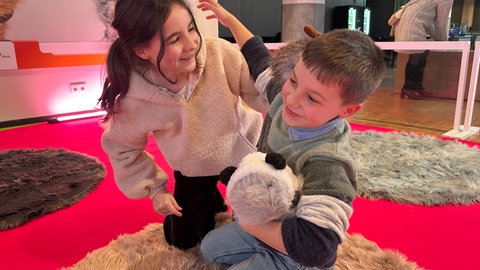 Zwei Kinder spielen mit meerschweinchenartigen Robotern des Elektronischen Streichelszoos im ZKM. Sie sollen so den Umgang mit KI lernen.
