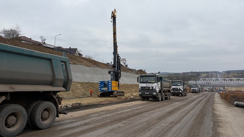 Die Baustelle auf der A8 bei Pforzheim: Sehr viele Lastwagen stehen in einer Reihe und ein riesiger Bohrer macht seine Arbeit.