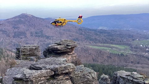 Ein Rettungshubschrauber zieht einen verletzten Kletterer am Battertfelsen mit einer Seilwinde nach oben. 