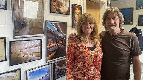 Manne Gelmar zusammen mit seiner Frau Claudia, die seit vielen Jahren im Betrieb mitarbeitet. Im Hintergrund die Fotowand mit einigen der Flugzeugausstattungen, an deren Gestaltung Manne Gelmar und das Team beteiligt waren. 