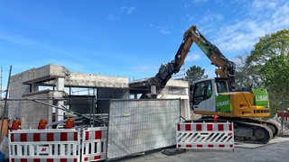 Abriss Turmbergbahn in Karlsruhe-Durlach: Ein gelber Bagger reißt ein Stück aus dem Gerippe eines grauen Betongebäudes.
