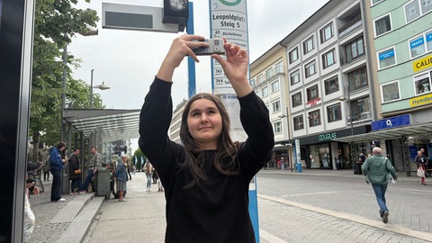 Eine Schülerin steht auf dem Leopoldplatz in Pforzheim und macht ein Foto mit dem Handy.