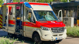 Ein Krankenwagen steht an einer Straße. Die Windschutzscheibe ist beschädigt. Der Rettungswagen ist mit einem Fahrradfahrer zusammengestoßen.