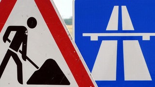 Ein Baustellenschild ist vor einem Autobahnschild platziert.