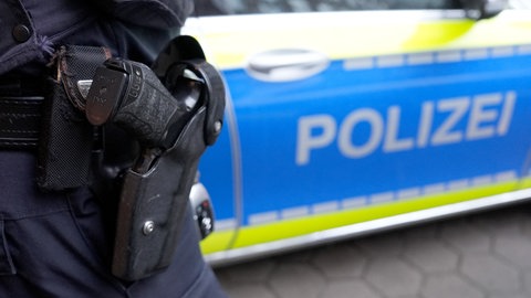 Polizist mit Dienstwaffe neben Polizeiwagen 