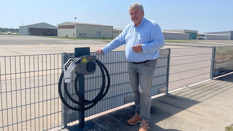 Dirk Eggert, Betreiber des City-Flugplatzes in Mannheim, steht neben einer Ladesäule für E-Flugzeuge.