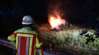 Ein Feuerwehrmann beobachtet, wie weitere Einsatzkräfte ein Feuer auf einem Feld löschen.