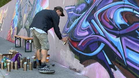 Der Graffiti-Künstler sprüht einen Schriftzug in blau, lila und rot.