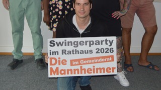 Der Stadtrat Julien Ferrat mit einem Schild "Swingerparty im Rathaus"