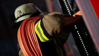 Eine Einsatzkraft der Feuerwehr nimmt einen Schlauch aus einem Einsatzfahrzeug der Feuerwehr (Symbolbild).