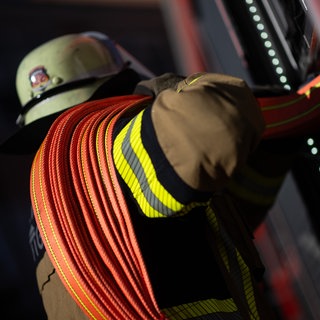 Eine Einsatzkraft der Feuerwehr nimmt einen Schlauch aus einem Einsatzfahrzeug der Feuerwehr (Symbolbild).