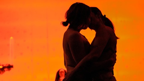 Zwei Frauen umarmen sich bei der Aufführung der Opernperformance "Sancta", während im Hintergrund Nonnen zu sehen sind.