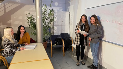 Iryna Verbivska steht vor einem Whiteboard mit drei Schülerinnen aus der Ukraine, ihnen bringt sie Deutsch bei.
