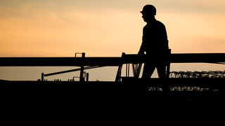 Die Silhouette eines Bauarbeiters zeichnet sich auf einer Baustelle vor dem verfärbten Morgenhimmel ab (Symbolbild). In holzgerlingen können junge Menschen bei einem Freiwilligen Handwerksjahr in verschiedene Handwerksberufe reinschnuppern. Das soll Orientierung bieten und führt vielleicht sogar zum Traumjob.
