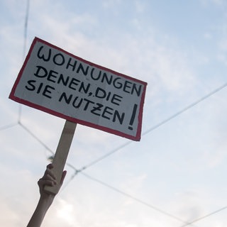 Eine Frau hält bei einer Demonstration gegen Wohnungsnot ein Schild hoch mit der Aufschrift "Wohnungen denen, die sie nutzen!".