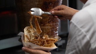 Ein Mann füllt ein Fladenbrot mit Fleisch von einem Dönerspieß. Der Spieß wurde von der Firma Birtat produziert.