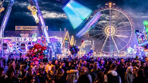 Viele Menschen sind am Abend zwischen Zelten und Fahrgeschäften auf dem Cannstatter Volksfest.