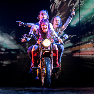 Drei Mitwirkende des Queen-Musicals "We will rock  you" sitzen auf einem Motorrad und fahren über die Bühne in Stuttgart. 