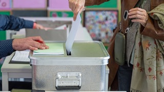 Eine Frau steckt ihren Stimmzettel in eine Wahlurne (Symbolbild).