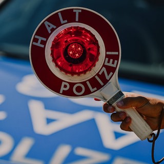 Eine Polizeikelle vor einem Streifenwagen (Symbolbild). In Deggingen (Kreis Göppingen) hat die Polizei ein Auto mit acht unangeschnallten Kindern entdeckt.