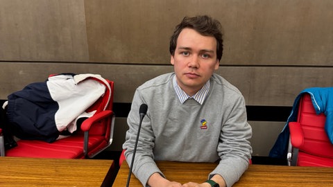 Gleb sitzt an einem Pult und schaut in die Kamera