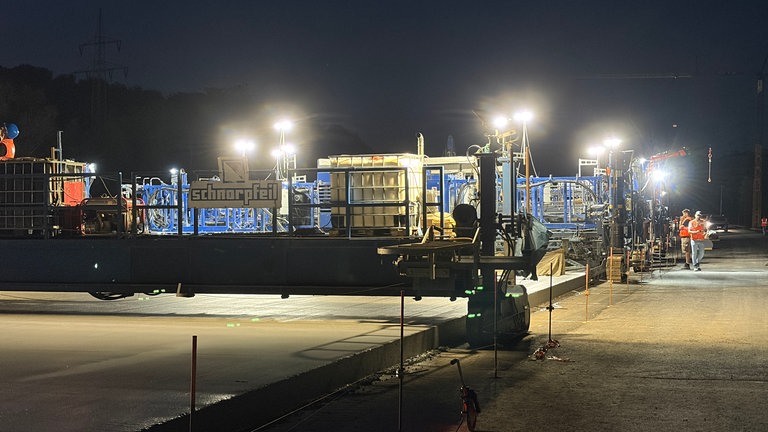 Die riesige Maschine, der Betonfertiger, wälzt den frischen, neuen Beton aus.