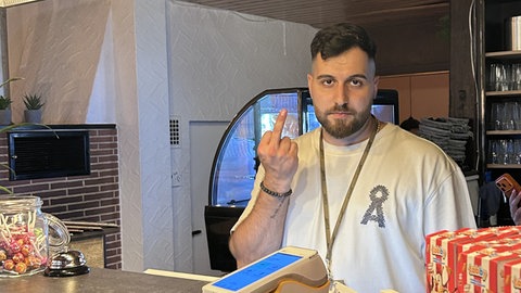 Inhaber Serdar Bingöl steht hinter dem Tresen und zeigt einen Stinkefinger